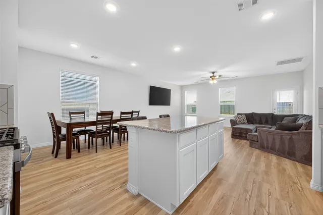 a large living room with stainless steel appliances kitchen island granite countertop a large center island and a wooden floor
