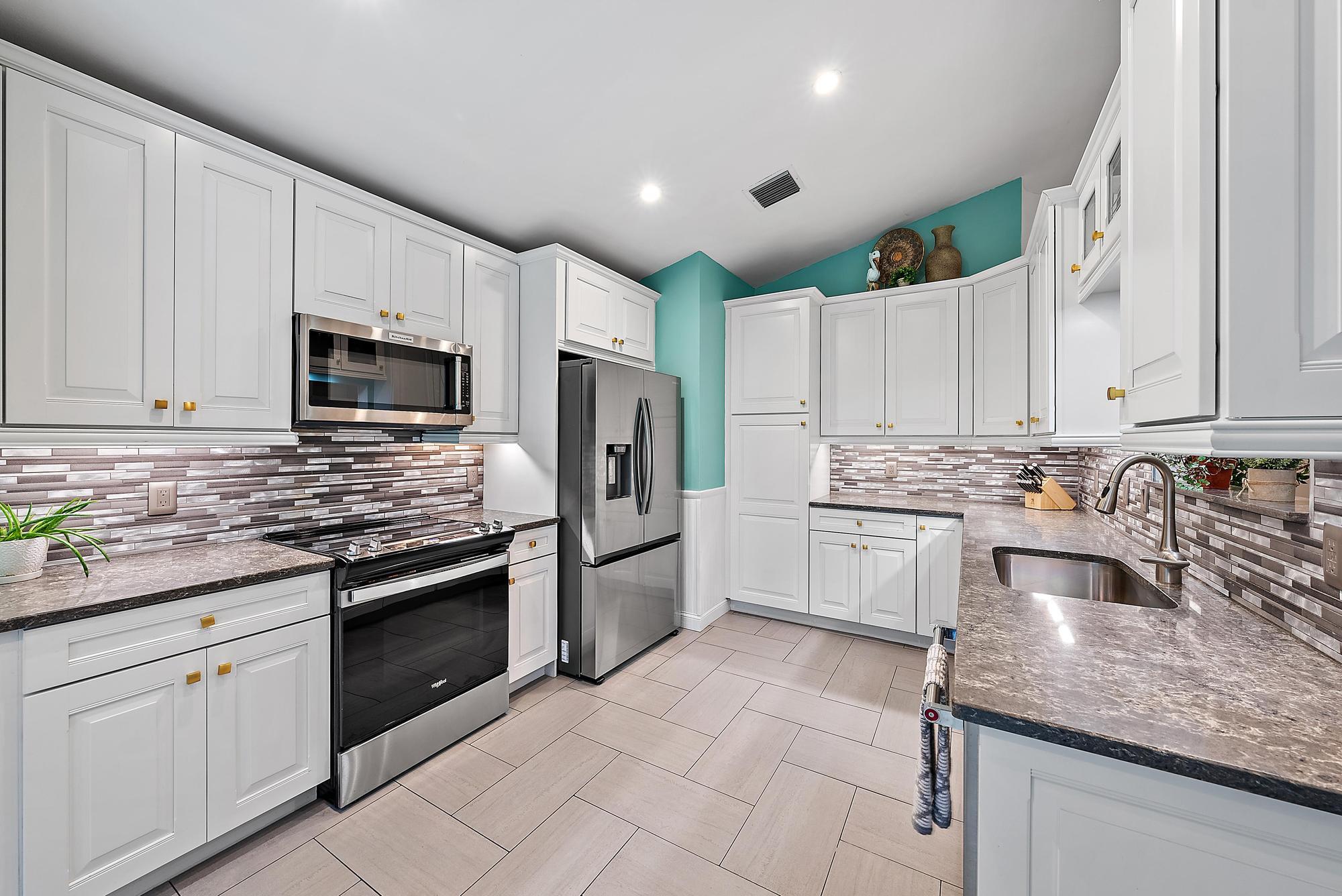 112 Spoonbill Court Jupiter, FL 33458 - Photo 4 of 28 a kitchen with kitchen island granite countertop white cabinets white stainless steel appliances and a sink