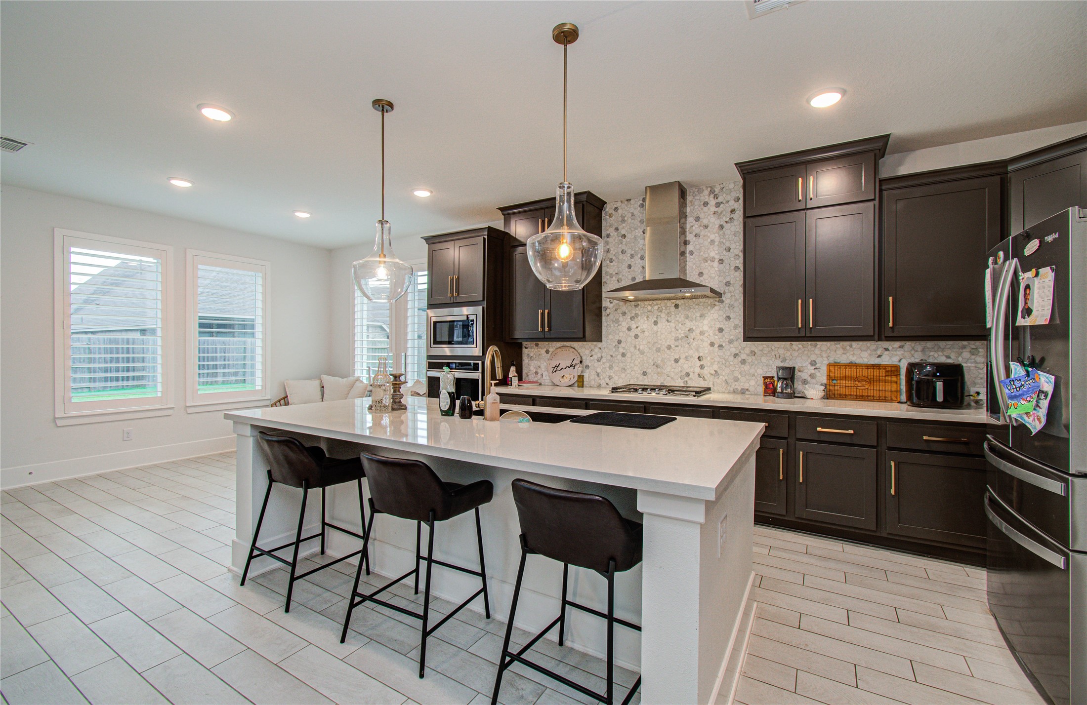 4211 Limestone Terrace Manvel, TX 77578 - Photo 7 of 33 This modern kitchen features sleek dark cabinetry, a large central island with seating, stainless steel appliances, and elegant pendant lighting. The open layout and bright windows create a spacious and inviting atmosphere.