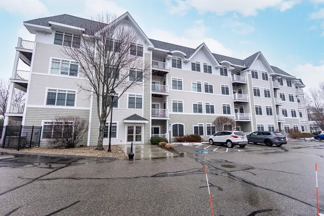 a front view of a building with lot of cars and trees