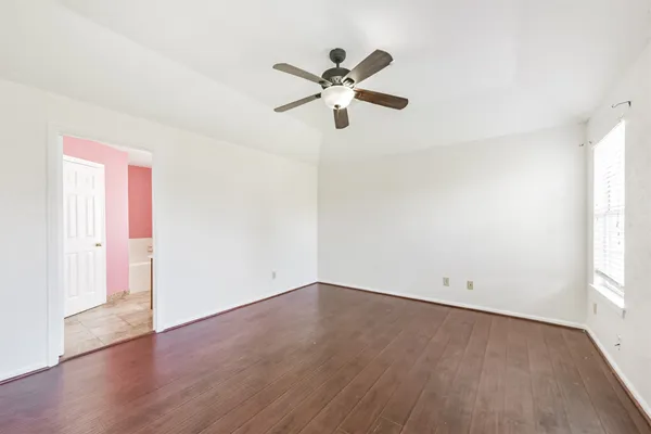 an empty room with wooden floor fan and windows