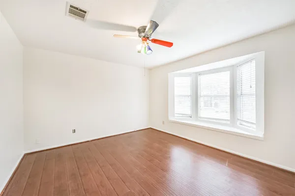 an empty room with wooden floor ceiling fan and windows