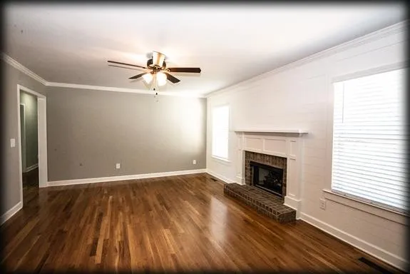 an empty room with wooden floor fireplace and windows