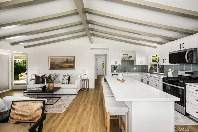a living room with stainless steel appliances furniture a rug and a kitchen view