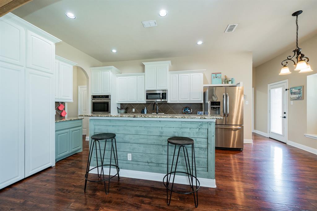 14176 Paterson Road Talty, TX 75126 - Photo 9 of 40 a kitchen with kitchen island granite countertop wooden floors and refrigerator