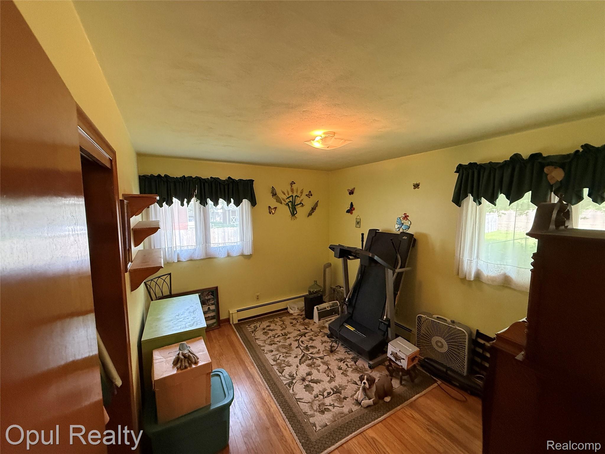 7899 Ida East Road Ida, MI 48140 - Photo 32 of 48 Room featuring wood-finish flooring, two windows with valances and sheer curtains, a flush-mount ceiling light fixture, and a baseboard heating element