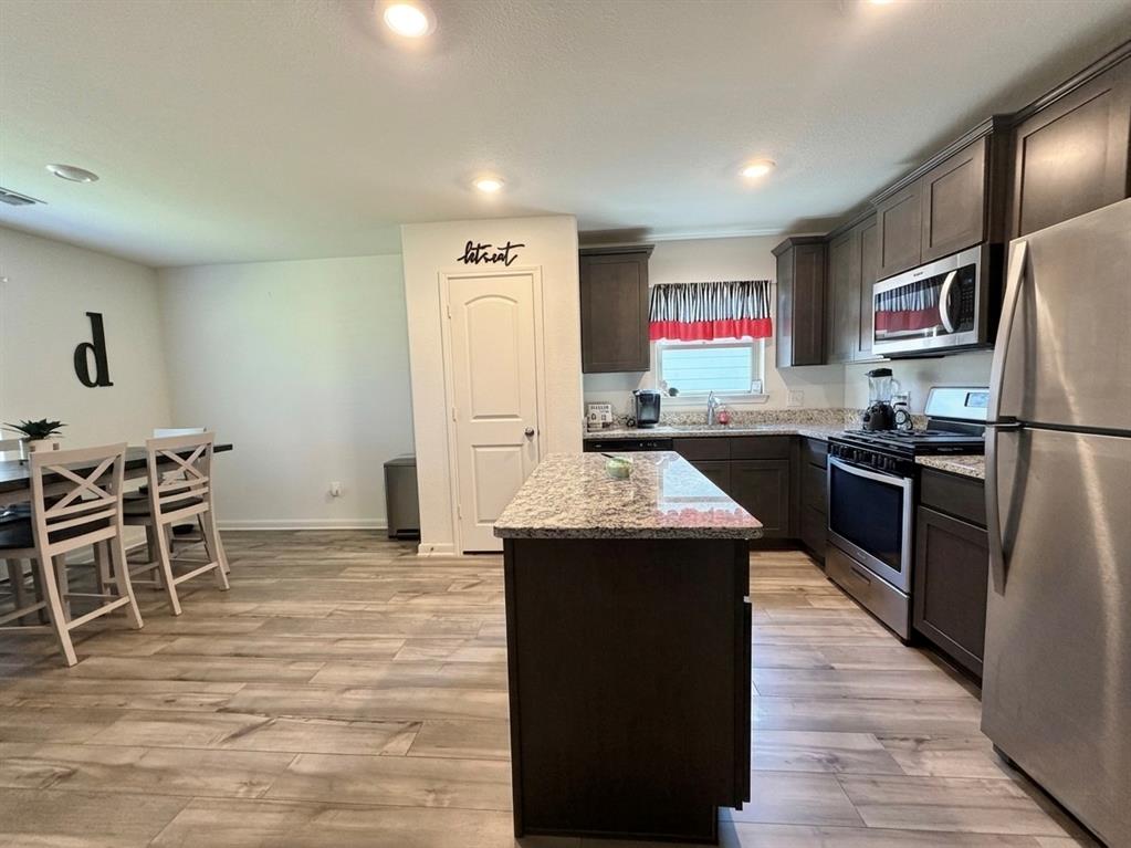 13604 Mineral Road Ponder, TX 76259 - Photo 4 of 20 Kitchen with stainless steel appliances, a kitchen island, dark wood finish cabinets, light stone countertops, and light wood finished floors