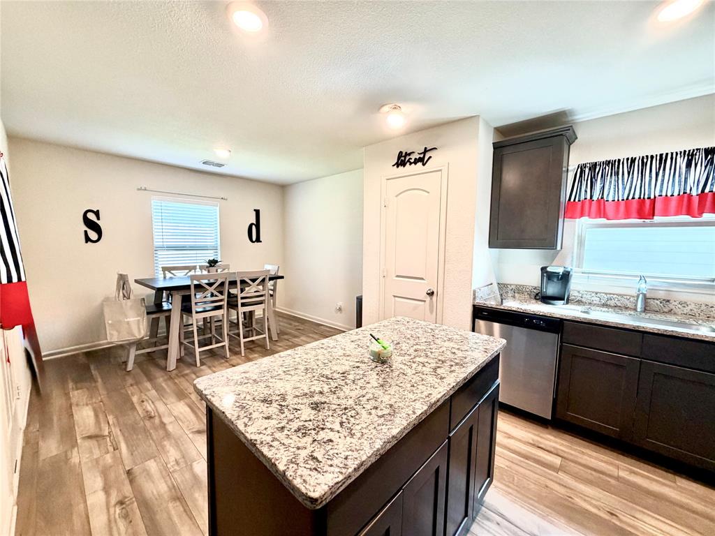 13604 Mineral Road Ponder, TX 76259 - Photo 5 of 20 Kitchen featuring dark wood finish cabinetry, a center island, stainless steel dishwasher, light stone counters, and light wood finished floors