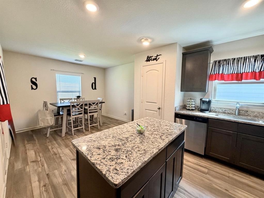 13604 Mineral Road Ponder, TX 76259 - Photo 8 of 20 Kitchen featuring dark wood finish cabinetry, a kitchen island, stainless steel dishwasher, light stone countertops, and light wood-style flooring