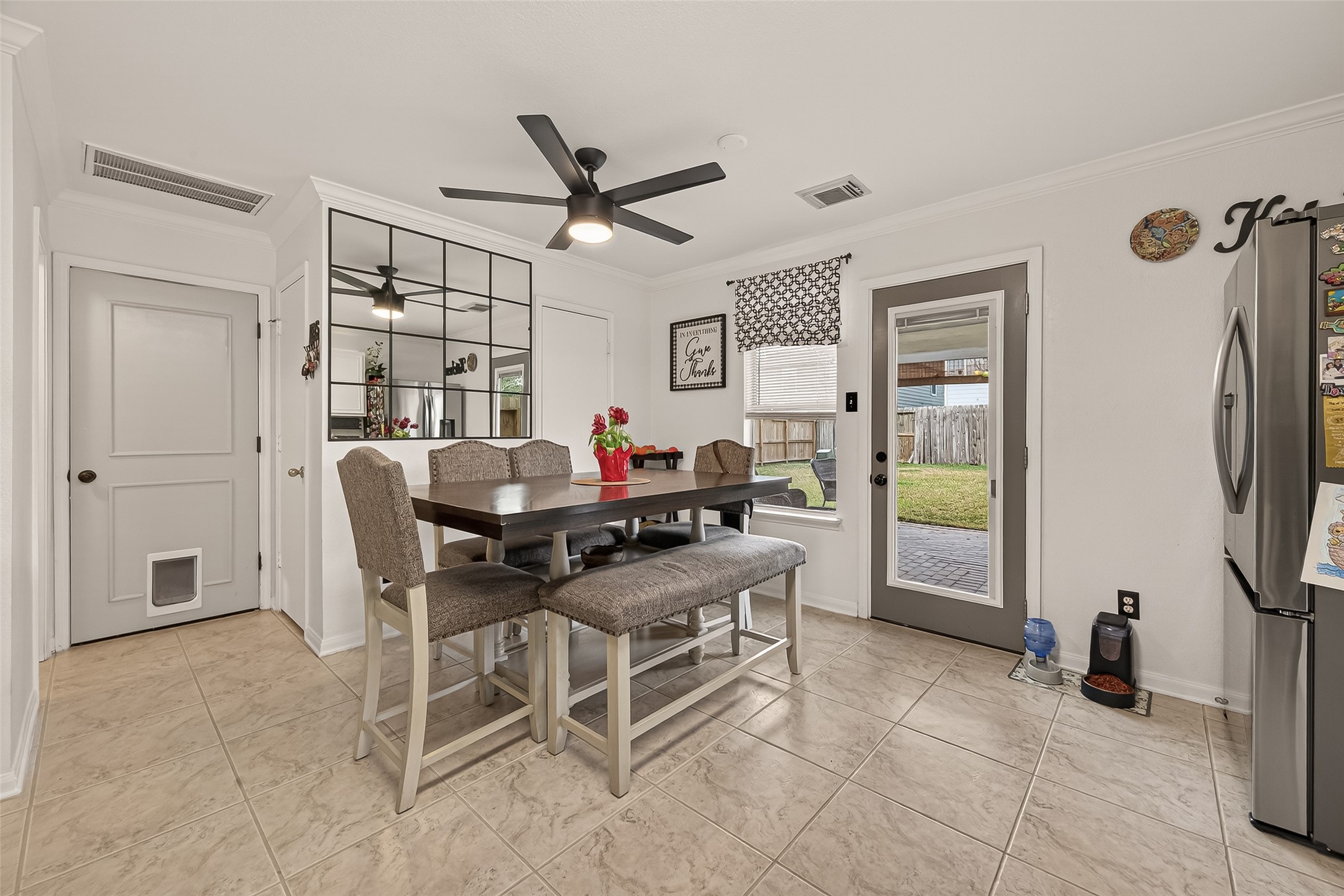 9902 Victoria Point Lane Houston, TX 77075 - Photo 8 of 35 Bright dining area with tile flooring, modern ceiling fan, and a large mirror. Features a cozy table set for four, adjacent to a window and glass door leading to the backyard. Neutral tones create a welcoming atmosphere.