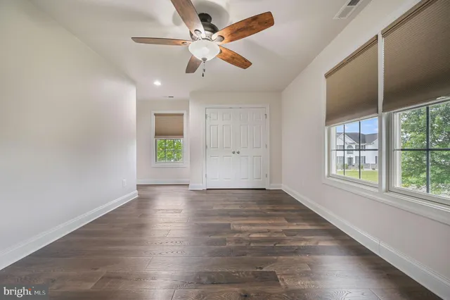 an empty room with wooden floor chandelier fan and windows