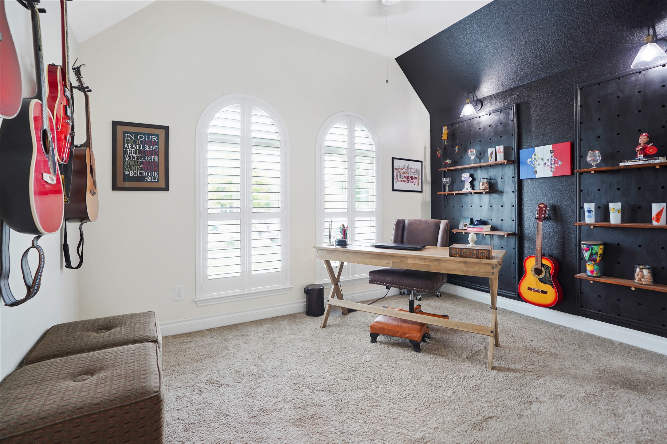 2345 Redwood Ridge Trail Manvel, TX 77578 - Photo 33 of 39 This bright home office features a vaulted ceiling, modern black accent wall with shelves, and ample natural light from arched windows. It includes a stylish desk and is accented with guitars, creating a creative and inviting workspace.