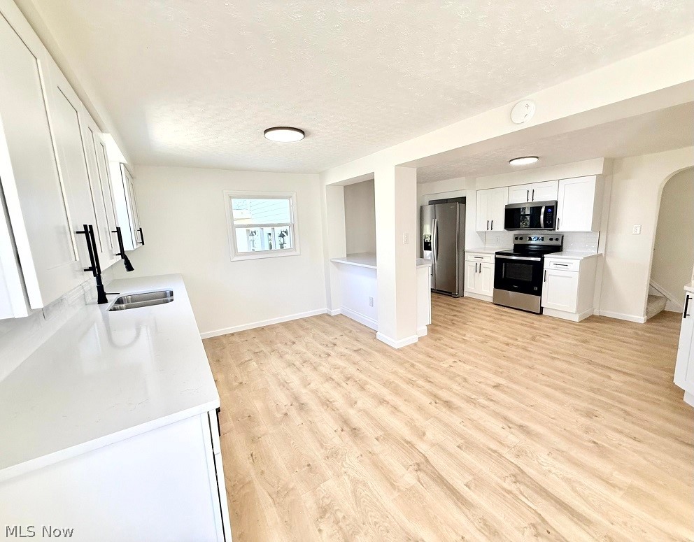 144 Aberdeen Road Steubenville, OH 43953 - Photo 11 of 34 Kitchen featuring white cabinetry, stainless steel appliances, arched walkways, light wood-type flooring, and a textured ceiling