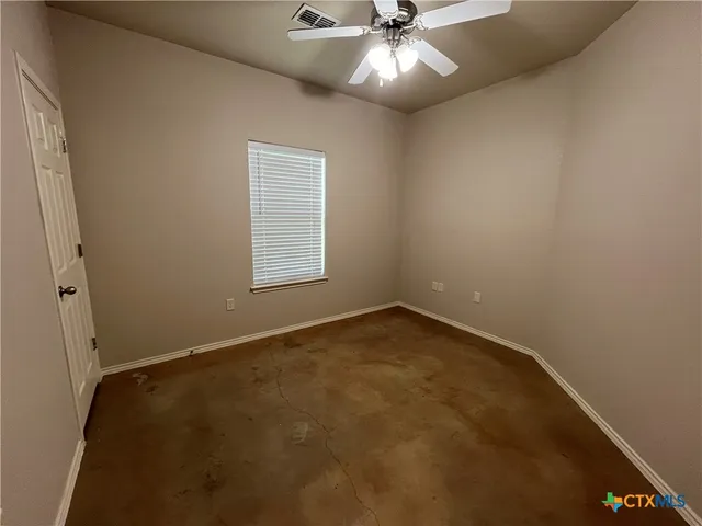 an empty room with a chandelier fan and windows