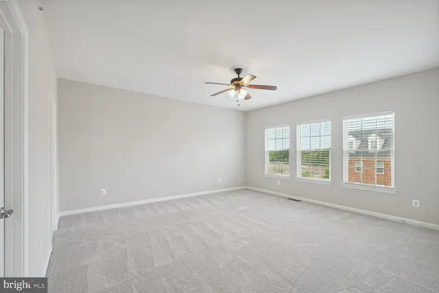 an empty room with chandelier fan and windows