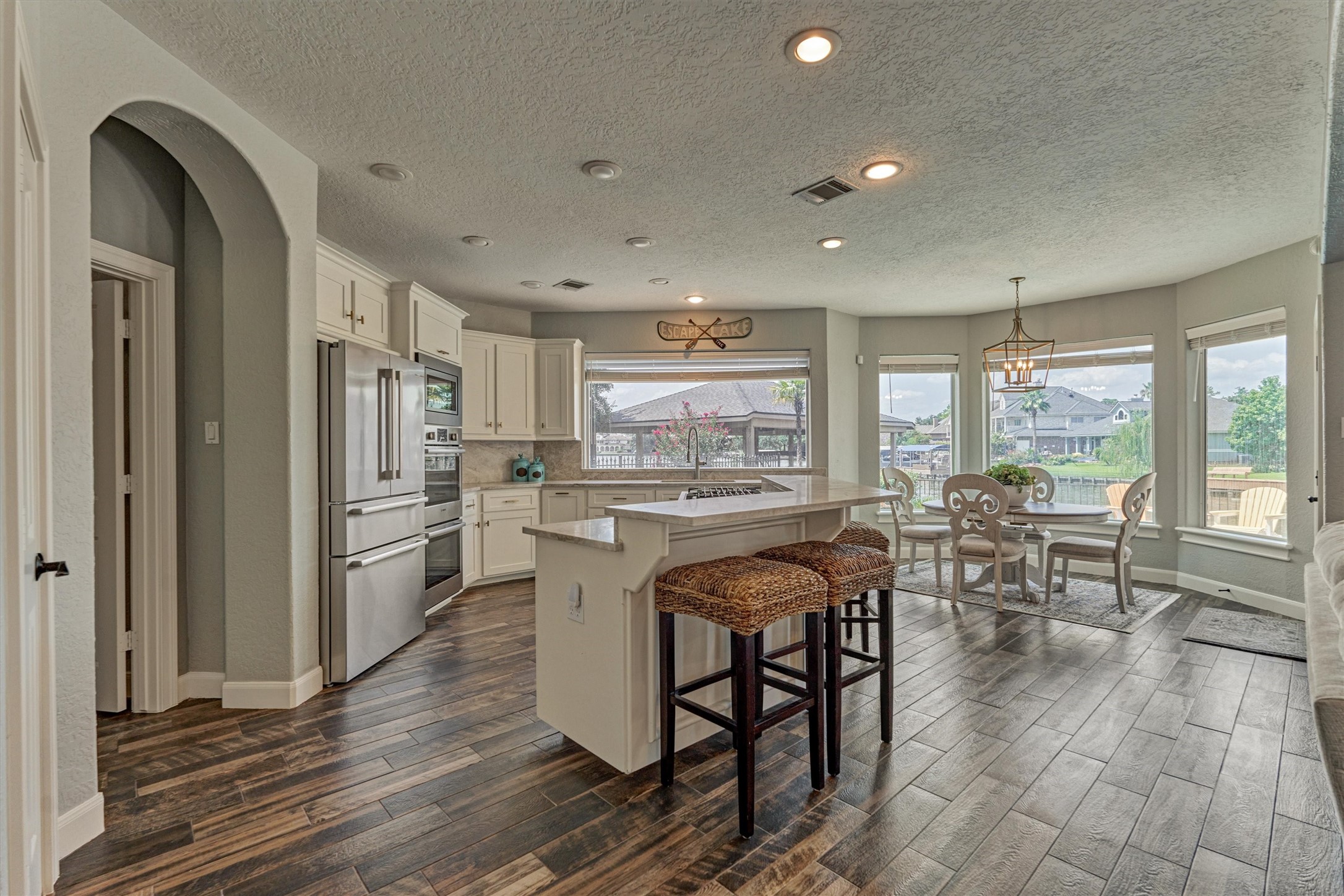 202 Edgemar Road Montgomery, TX 77356 - Photo 18 of 50 Bright kitchen with Taj Mahal quartzite bar height island, stainless steel appliances, and breakfast nook framed by wall-to-wall windows overlooking the pool and water views of the cove.
