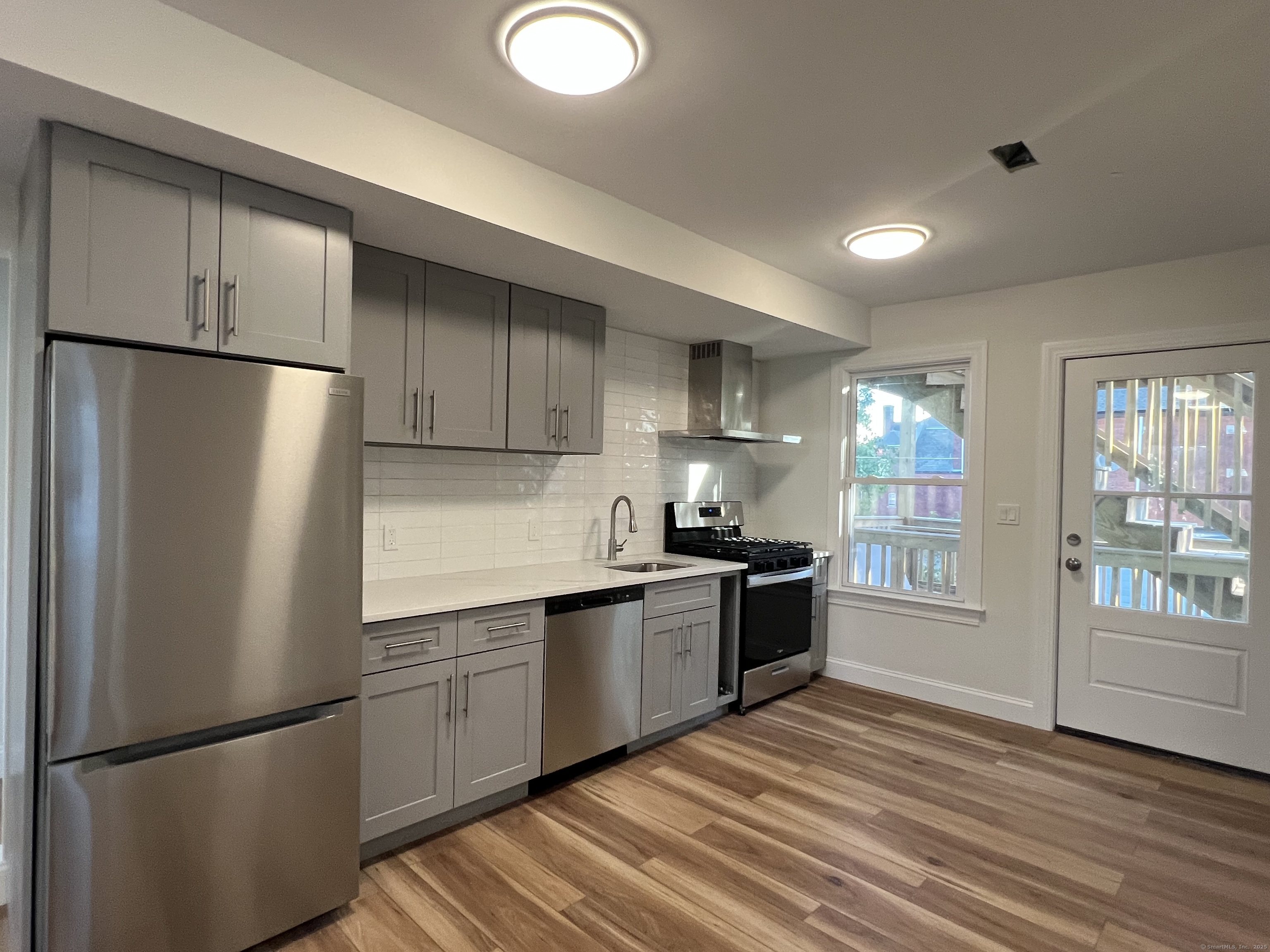 a kitchen with stainless steel appliances granite countertop a refrigerator a sink dishwasher a stove top oven a refrigerator and white cabinets with wooden floor