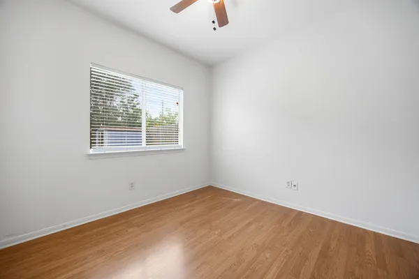 an empty room with wooden floor chandelier fan and windows