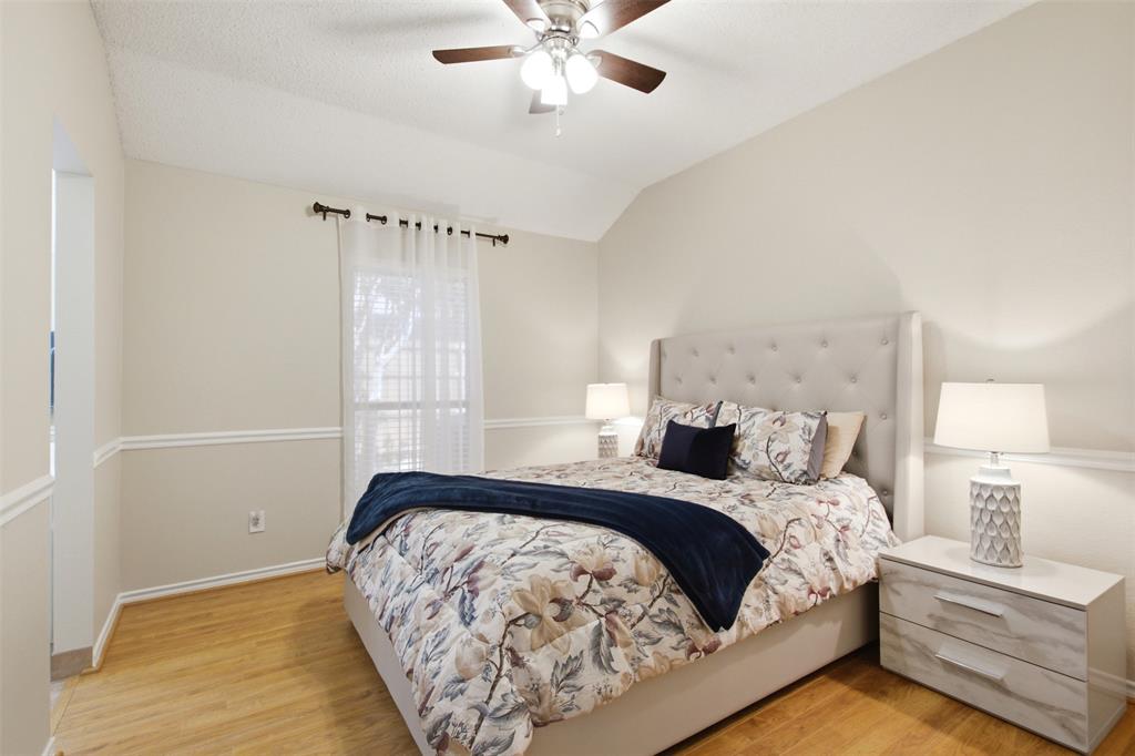 4218 Glistening Spring Rowlett, TX 75088 - Photo 24 of 39 Vaulted ceiling bedroom featuring wood-finish flooring, a window with sheer curtains, a ceiling fan with light fixture, and decorative wainscoting