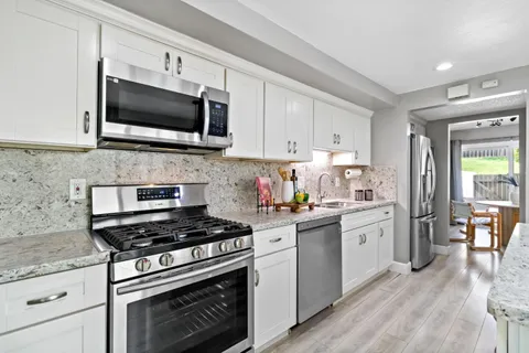 a kitchen with stainless steel appliances a sink dishwasher stove and microwave with wooden floor