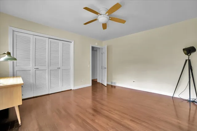 a view of an empty room with wooden floor and a ceiling fan
