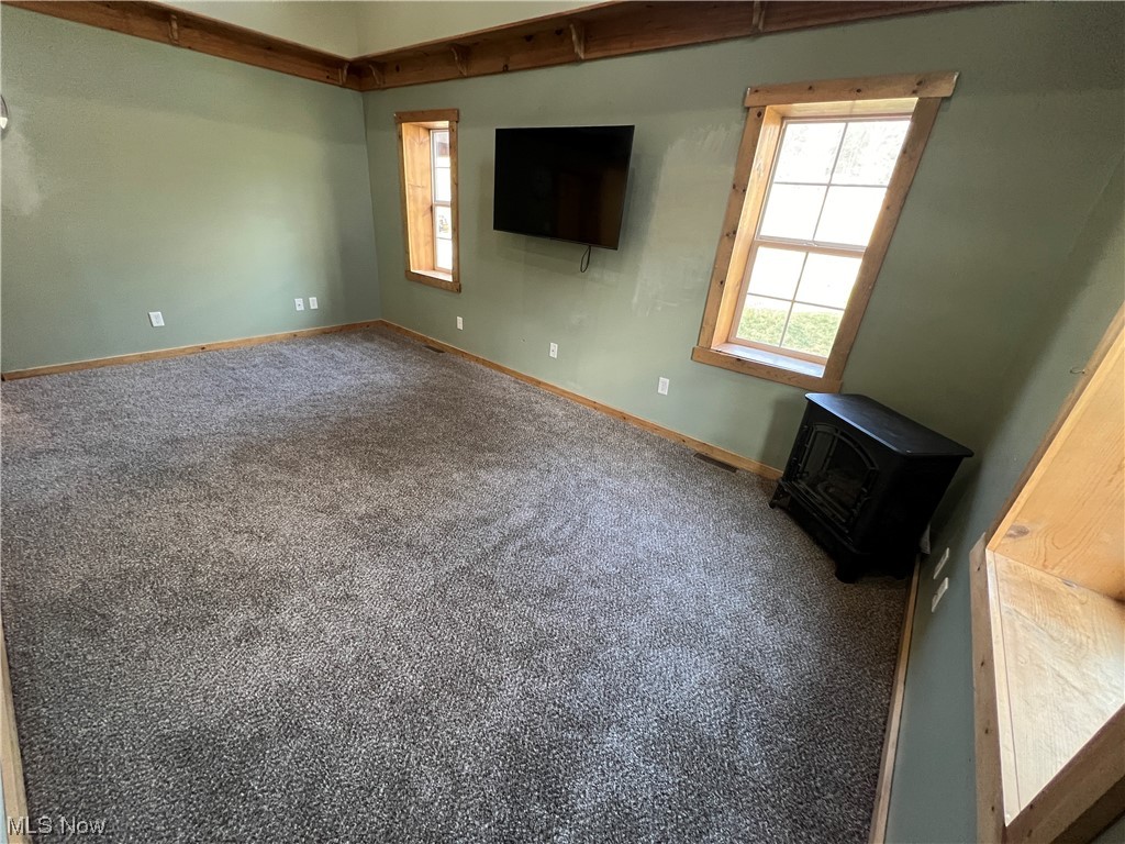 Unfurnished bedroom featuring carpet floors and a wood stove