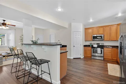 a kitchen with stainless steel appliances kitchen island granite countertop a stove top oven a sink a dining table and chairs with wooden floor