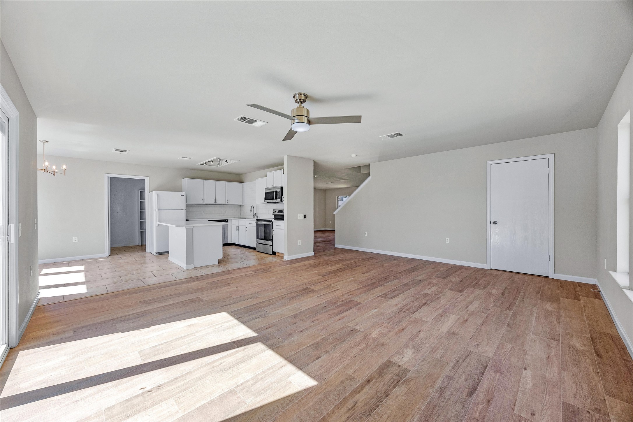 7541 Redrick Drive Austin, TX 78747 - Photo 16 of 40 Unfurnished living room with visible vents, baseboards, light wood-style floors, and ceiling fan with notable chandelier