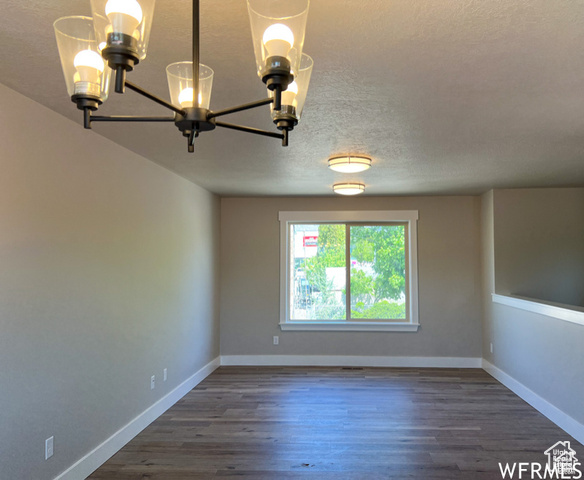 702 North 100 West Logan, UT 84321 - Photo 26 of 58 Spare room featuring dark wood-type flooring, a textured ceiling, baseboards, and a notable chandelier