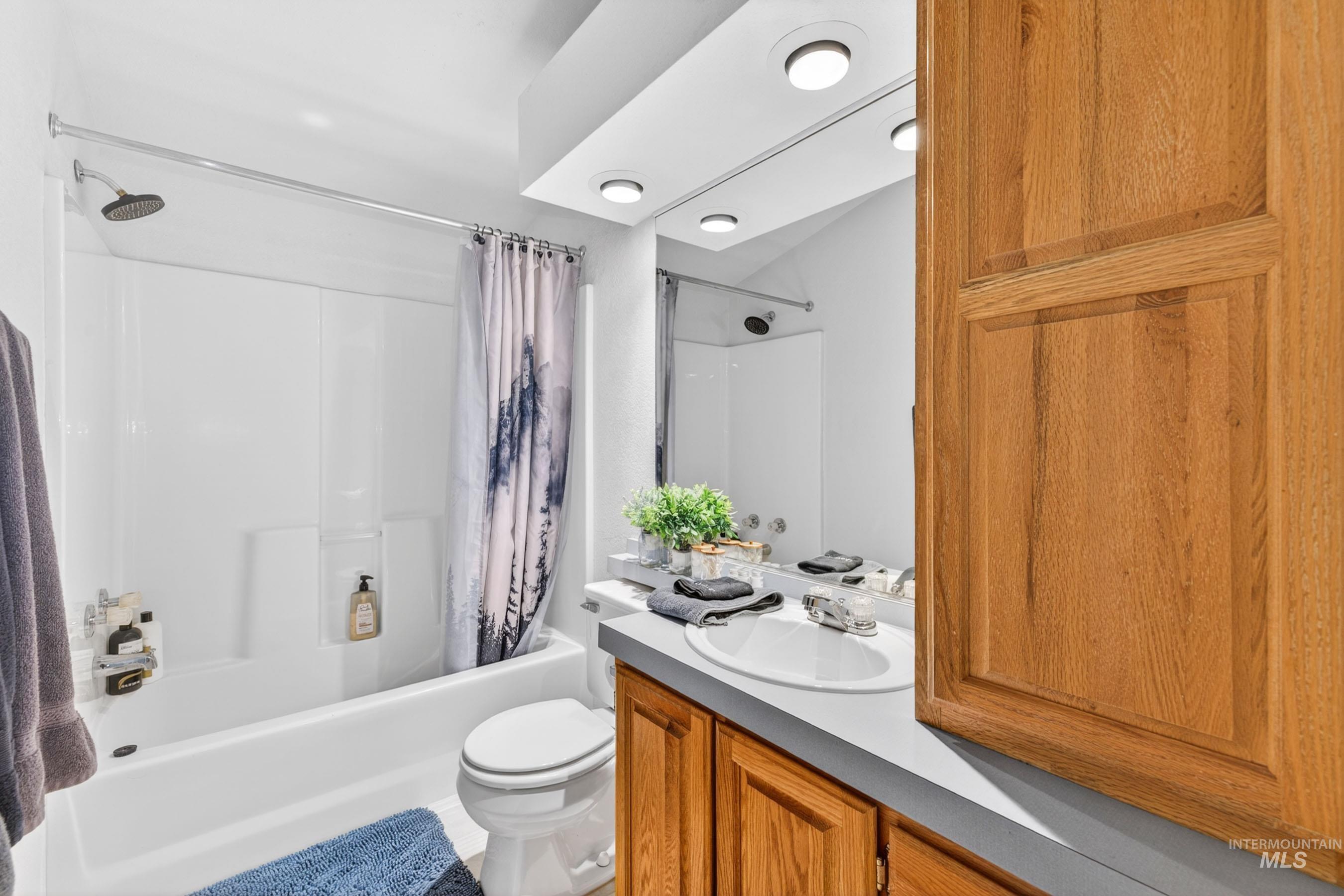 151 Cow Creek Road Lucile, ID 83542 - Photo 31 of 50 Bathroom featuring a white shower-over-tub combination with a rain showerhead, a single vanity with an integrated sink, a light-toned countertop, and wood-finish cabinetry