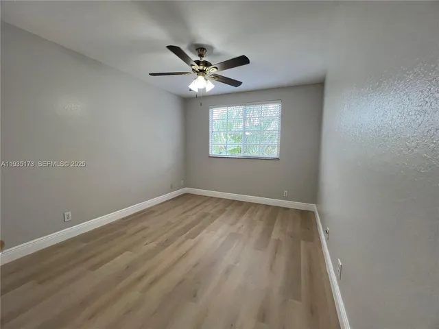 an empty room with wooden floor chandelier fan and windows