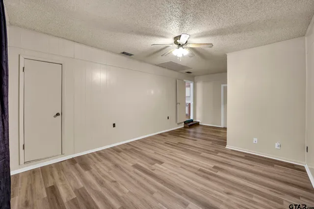 a view of an empty room with wooden floor and a ceiling fan