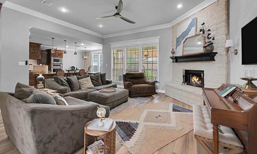 550 Hunton Lane Robinson, TX 76706 - Photo 5 of 35 Living room featuring light wood-style floors, ceiling fan, crown molding, a stone fireplace, and recessed lighting
