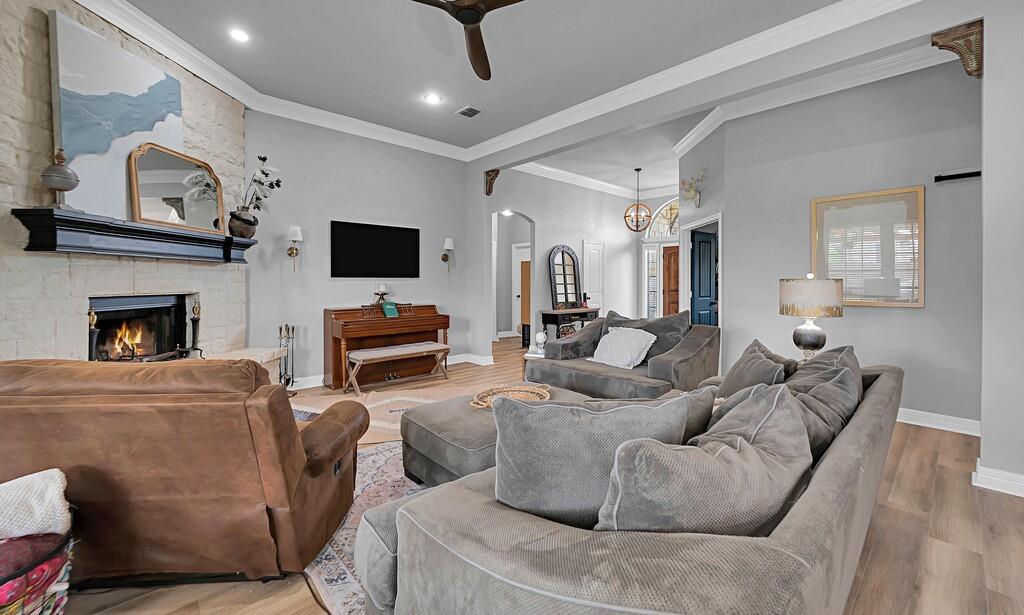 550 Hunton Lane Robinson, TX 76706 - Photo 7 of 35 Living area featuring a ceiling fan, a stone fireplace, wood finished floors, arched walkways, and ornamental molding