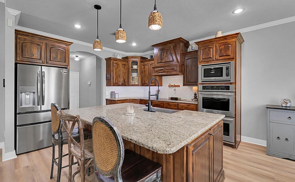 550 Hunton Lane Robinson, TX 76706 - Photo 8 of 35 Kitchen featuring stainless steel appliances, arched walkways, light wood finished floors, light stone countertops, and ornamental molding