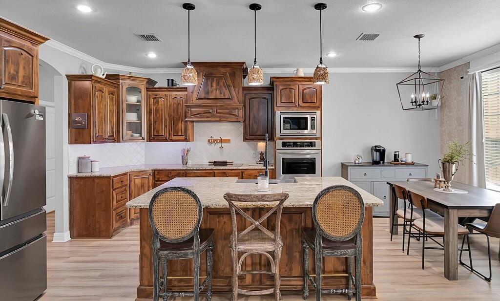 550 Hunton Lane Robinson, TX 76706 - Photo 9 of 35 Kitchen featuring appliances with stainless steel finishes, light wood-type flooring, crown molding, backsplash, and light stone counters