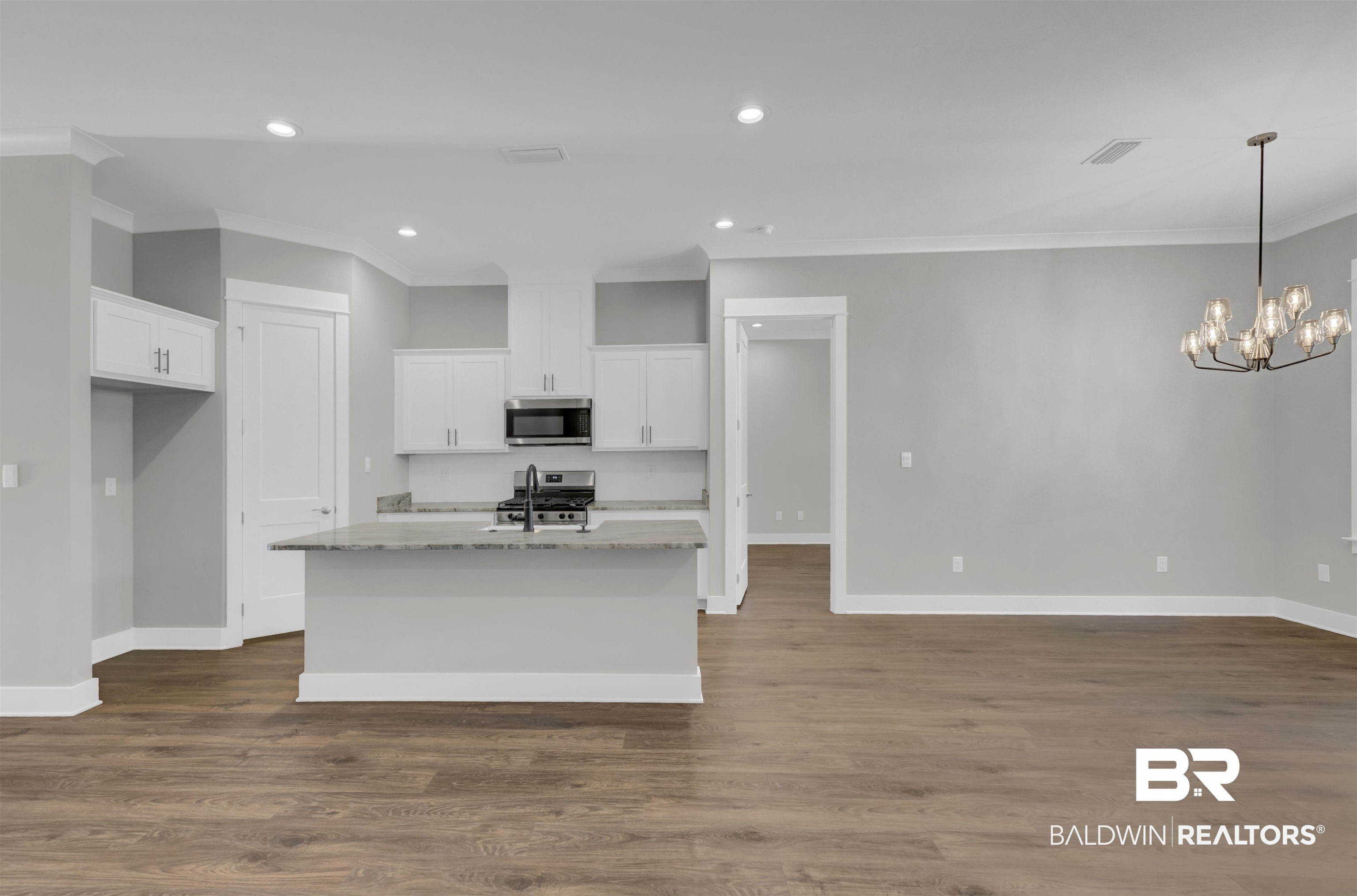 571 Morning Mist Way Fairhope, AL 36532 - Photo 13 of 47 Kitchen featuring light stone counters, white cabinets, a chandelier, ornamental molding, and a kitchen island with sink