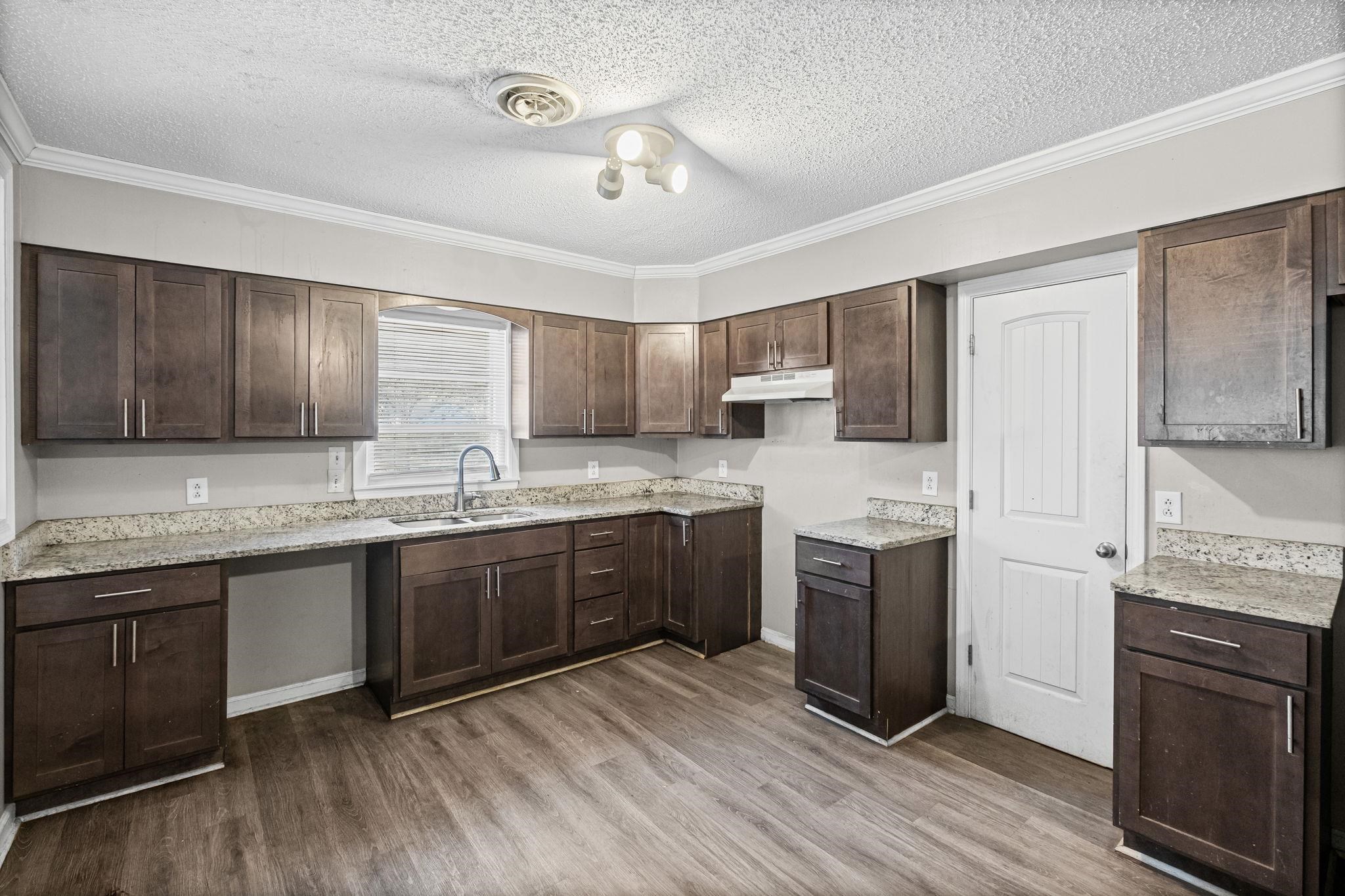4202 Reed Avenue Memphis, TN 38108 - Photo 8 of 22 Kitchen with dark brown cabinets, a textured ceiling, ornamental molding, light stone counters, and dark wood finished floors