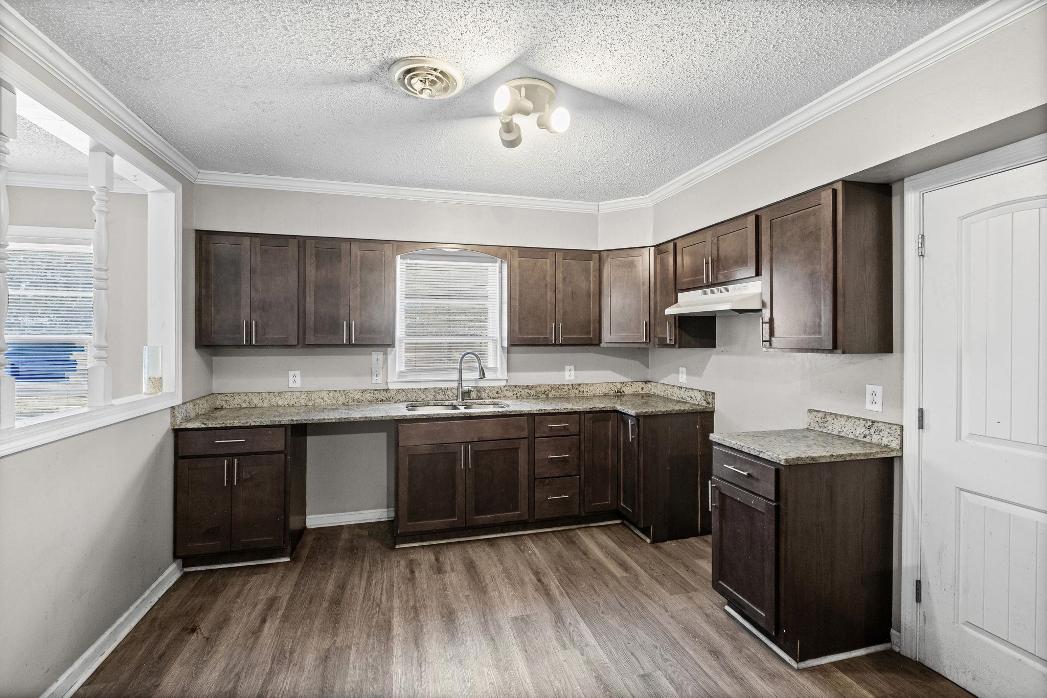 4202 Reed Avenue Memphis, TN 38108 - Photo 9 of 22 Kitchen featuring dark brown cabinetry, a textured ceiling, ornamental molding, dark wood-style flooring, and light stone countertops