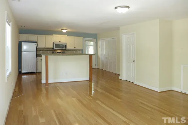 a view of kitchen and empty room with wooden floor