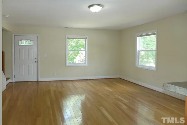 a view of an empty room with wooden floor and a window