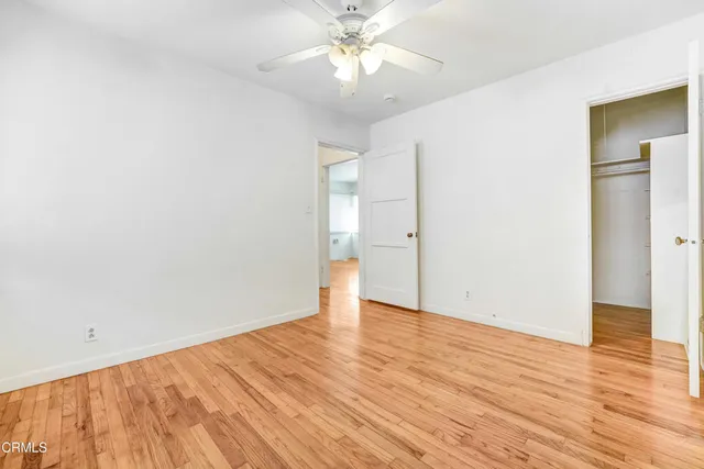 a view of an empty room with wooden floor and a ceiling fan