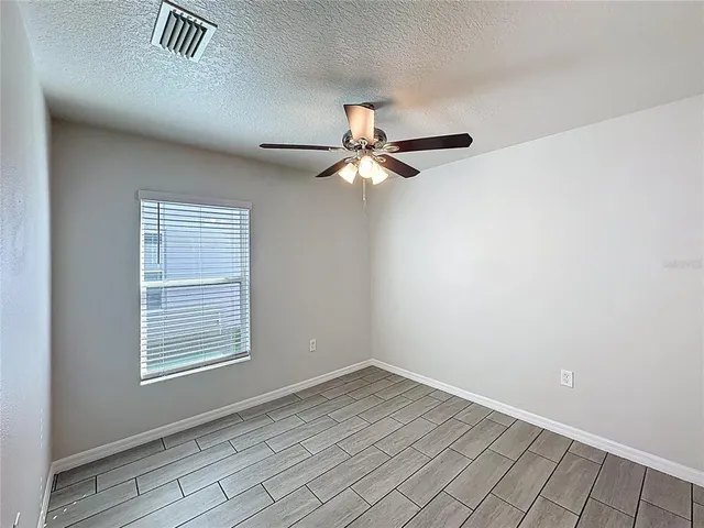 an empty room with wooden floor fan and windows