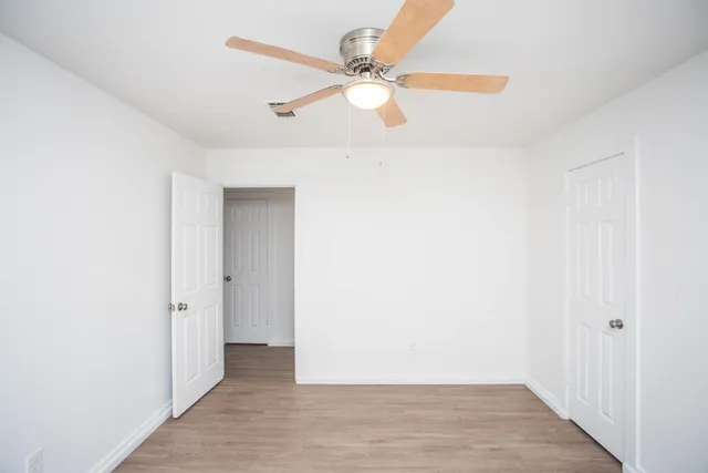 an empty room with wooden floor fan and windows