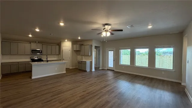 an empty room with wooden floor fan and windows