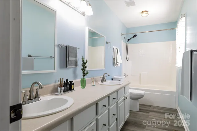 a bathroom with double vanity sink a mirror a toilet and a shower