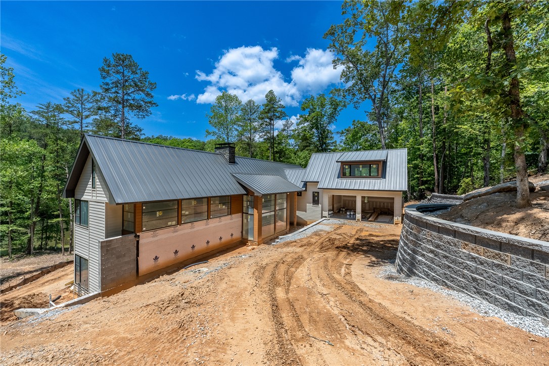A newly constructed modern home nestled in a wooded setting, featuring a sleek metal roof and an attached garage.
