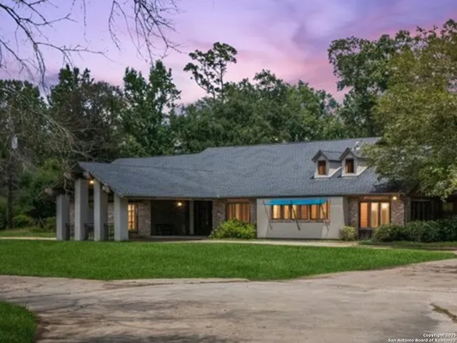 a view of a brick house with a large windows and a yard with plants and large trees