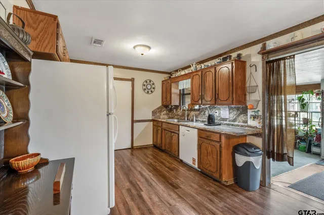 a kitchen with stainless steel appliances granite countertop a refrigerator a sink dishwasher a stove and white countertops with wooden floor