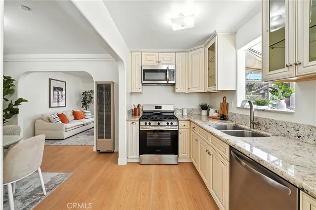 a kitchen with stainless steel appliances granite countertop a stove top oven a sink dishwasher and white cabinets with wooden floor